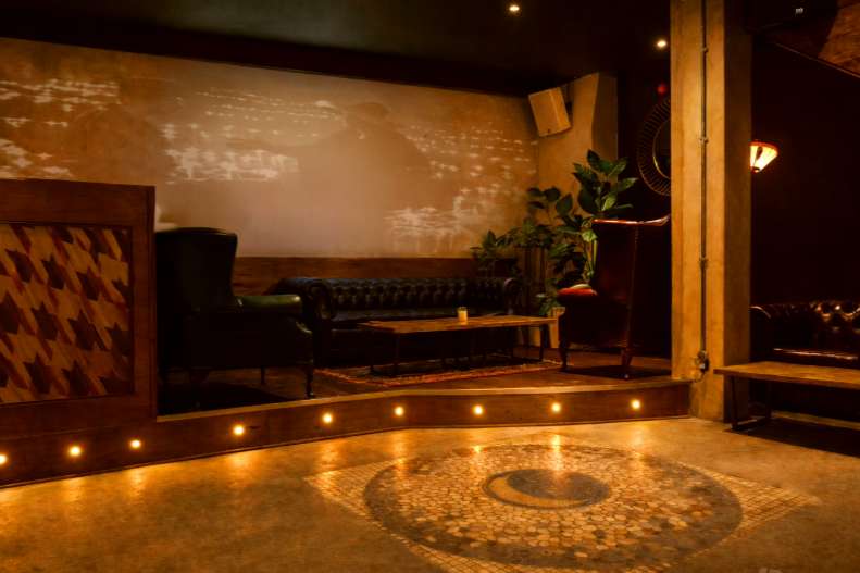 Modern lounge with polished concrete floor, ambient lighting, black leather seating, and projection screen on wall.