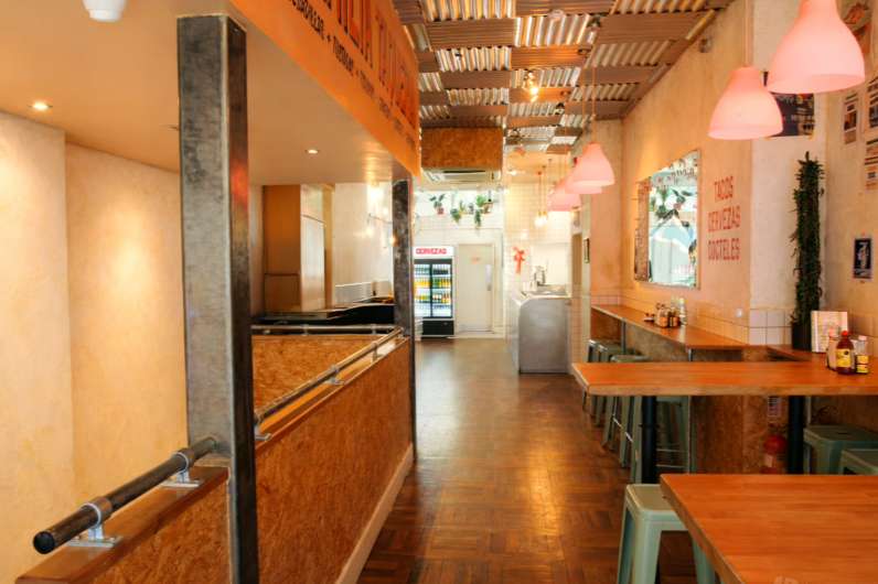 Restaurant interior with wooden counter, pink pendant lights, and industrial ceiling details.