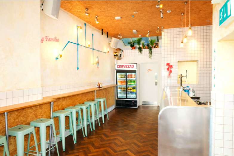 Casual bar counter with turquoise stools, beverage cooler, and decorative hanging plants under wooden ceiling.