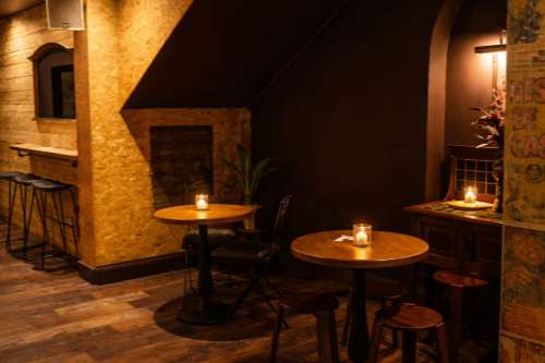 Intimate bar and lounge area with round tables, candlelit ambiance, exposed brick, and warm accent lighting.