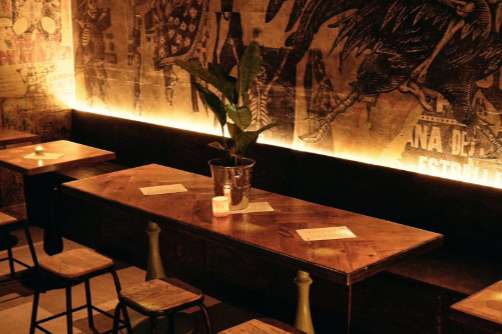 Interior dining space with long wooden table, bar seating, ambient lighting, and decorative wall art.