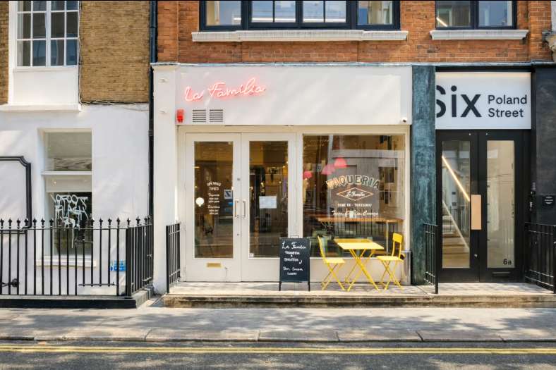 Exterior storefront of La Familia restaurant on Poland Street with brick facade, large windows, and yellow seating visible inside.
