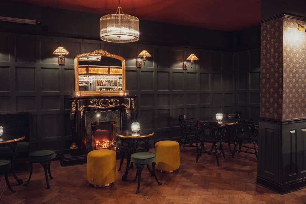 Upscale bar lounge with dark wood paneling, fireplace, gold accents, and ambient lighting. Seating arranged around low tables.