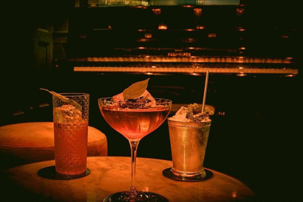 Three cocktails on a table with warm ambient lighting and dark background.