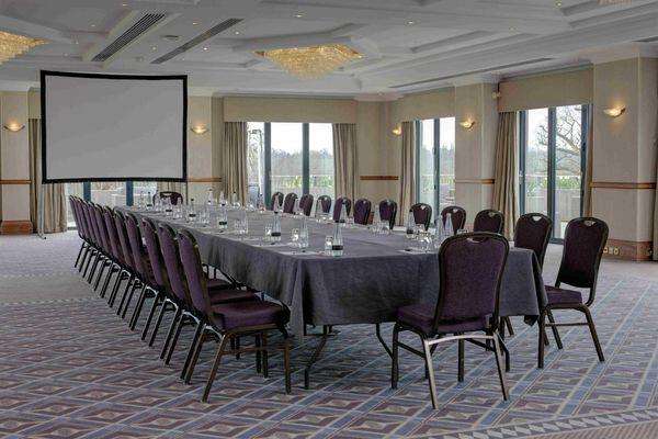 Conference room with long rectangular table, purple chairs, projection screen, and floor-to-ceiling windows.