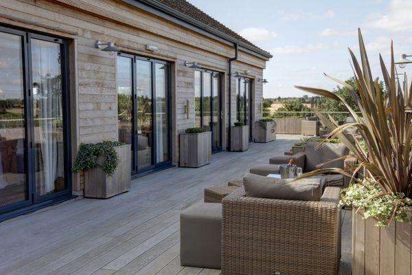 Outdoor terrace with rattan seating, potted plants, and countryside views under clear sky.