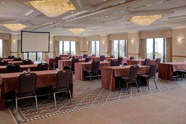 Conference room with round tables draped in burgundy linens, black chairs, projection screen, and decorative ceiling fixtures.