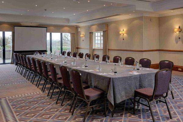 Windmill Suite set up with long boardroom-style table, burgundy chairs, projection screen, and recessed lighting.