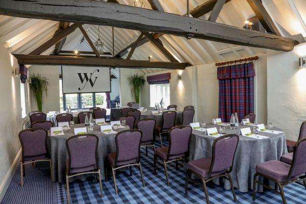 Windmill Suite set with round tables, purple chairs, grey linens, and exposed timber beams overhead.