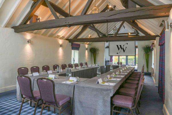 Meeting room with U-shaped table setup, purple chairs, exposed beam ceiling, and natural lighting.