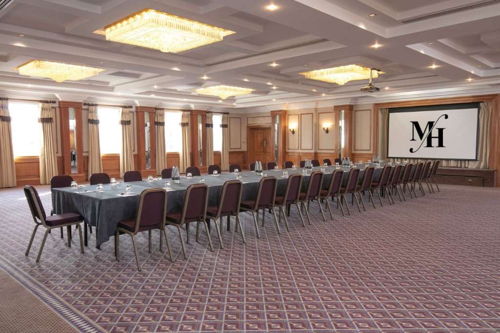 Conference room set with long boardroom table, burgundy chairs, coffered ceiling with recessed lighting, and projection screen.
