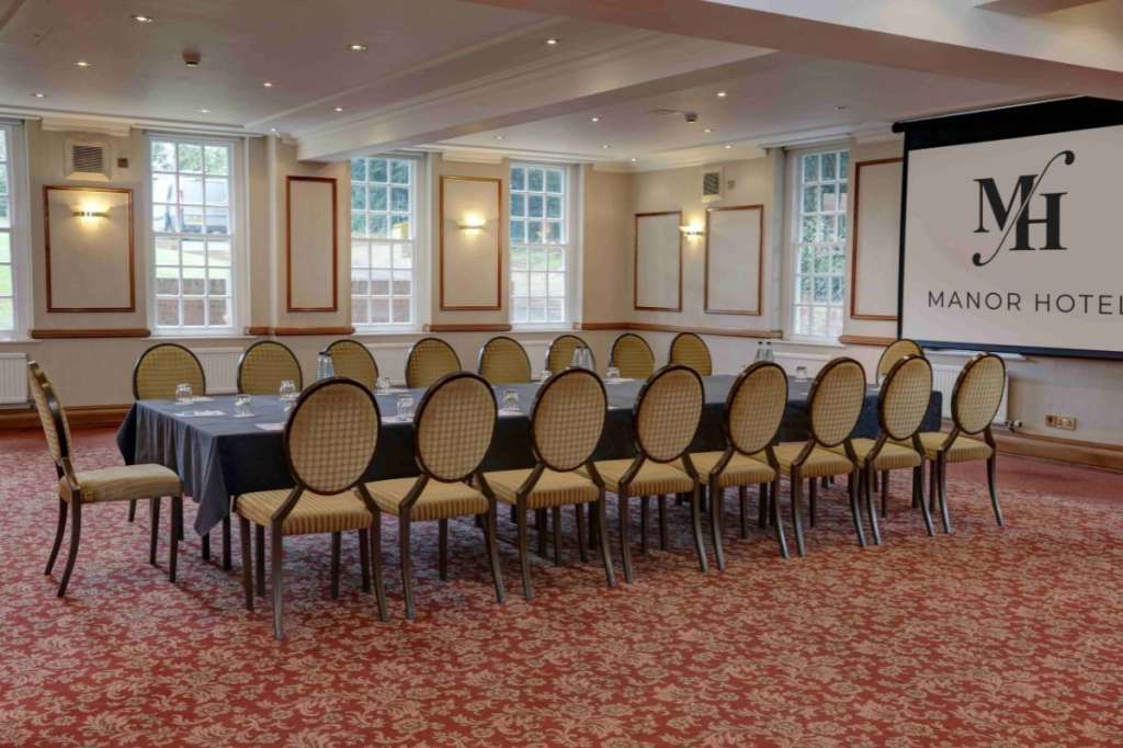 Meeting room with long rectangular table, upholstered chairs, projection screen, and large windows overlooking grounds.