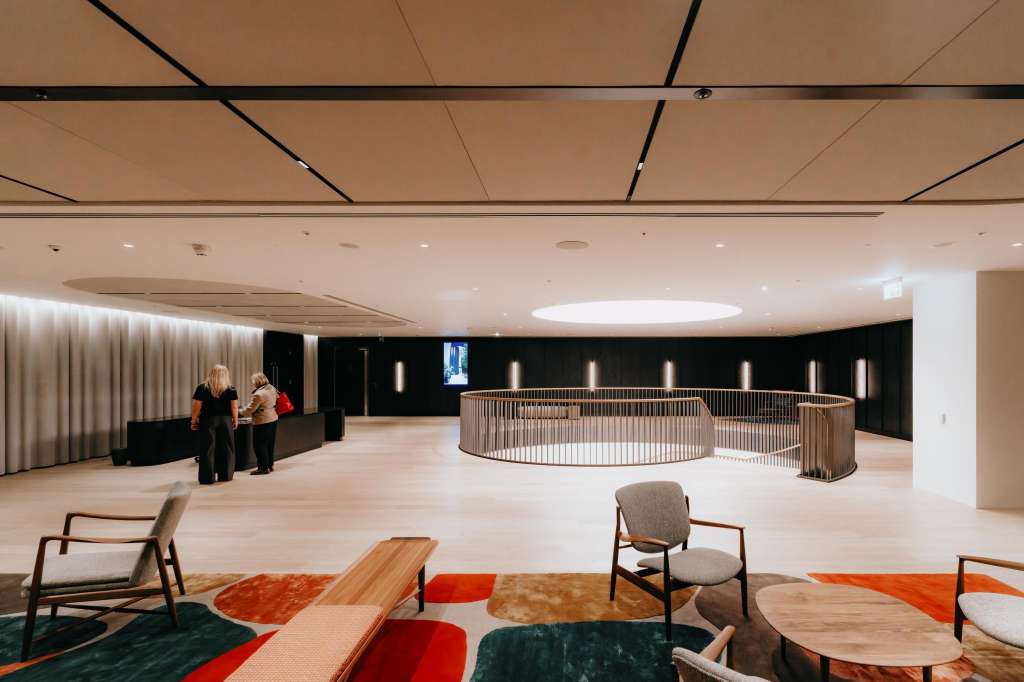 Modern open-plan space with curved wooden railings, contemporary seating, geometric rugs, and recessed ceiling lighting.