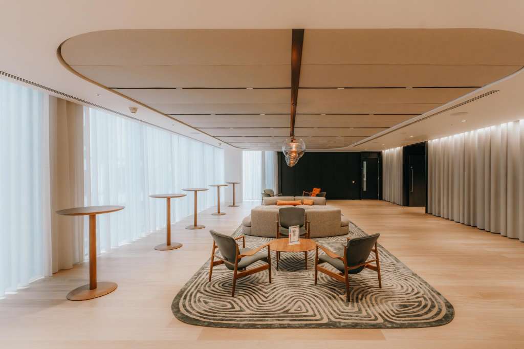 Modern atrium with lounge seating, geometric rug, floor-to-ceiling windows, and contemporary pendant lighting.