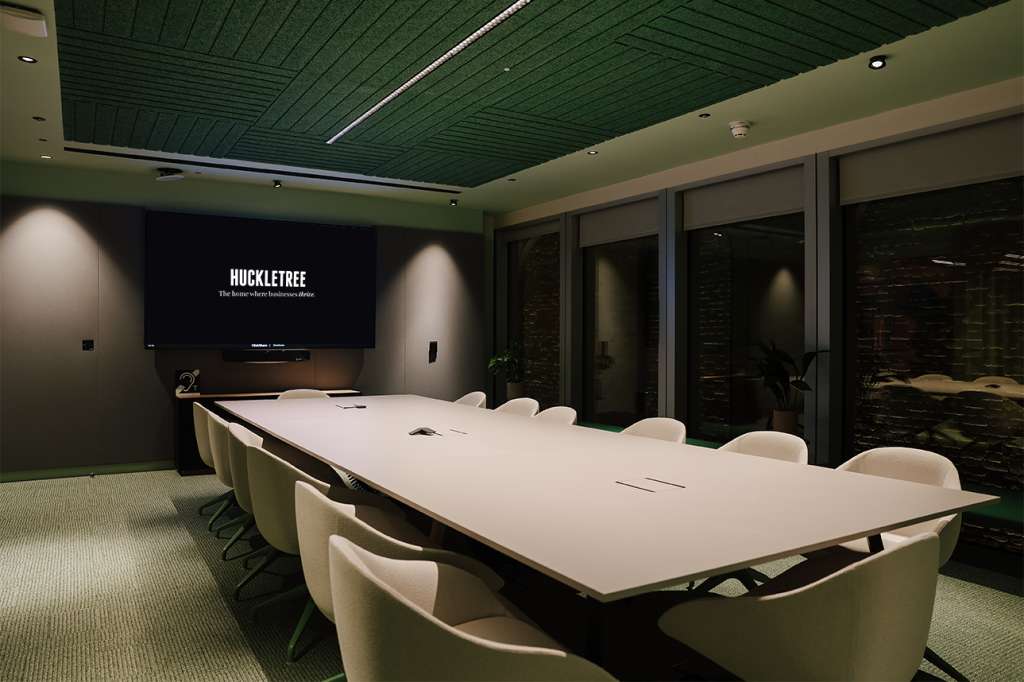 Modern conference room with long white table, cream chairs, green ceiling, and projection screen displaying Huckletree branding.