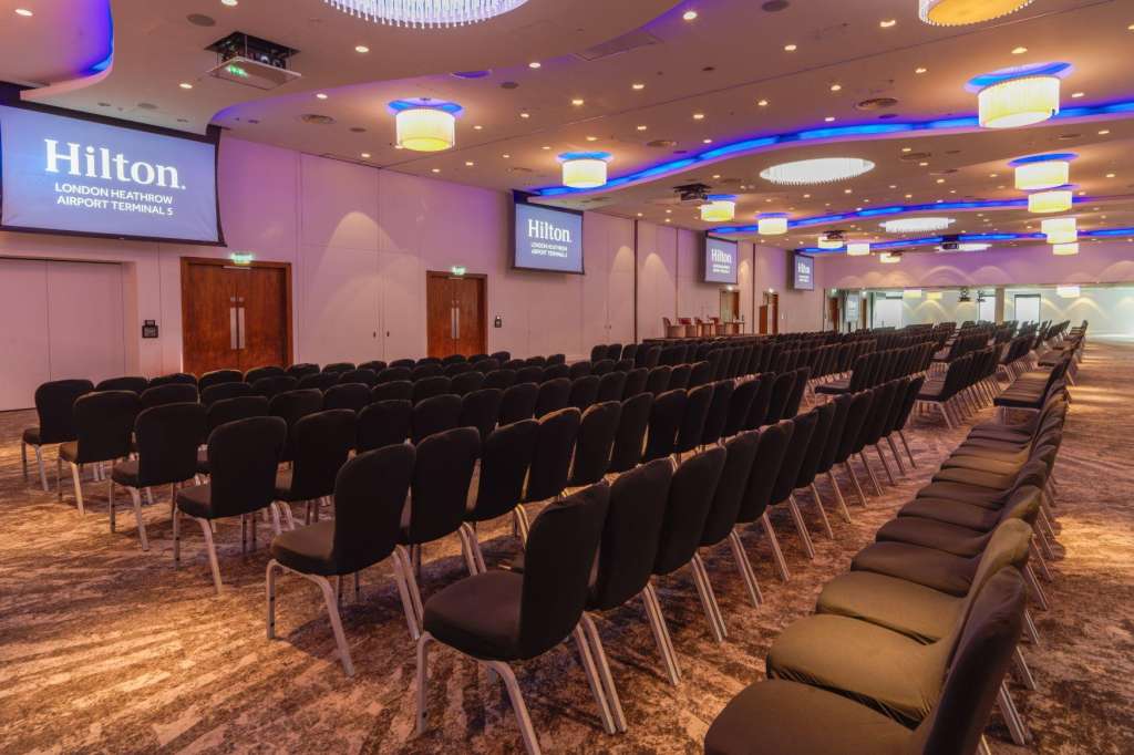The Ballroom set up with rows of black chairs facing projection screens, blue accent lighting, and recessed ceiling fixtures.