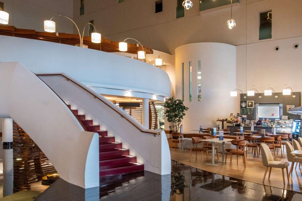 Modern atrium with curved staircase, wooden chairs, tables, and contemporary pendant lighting.