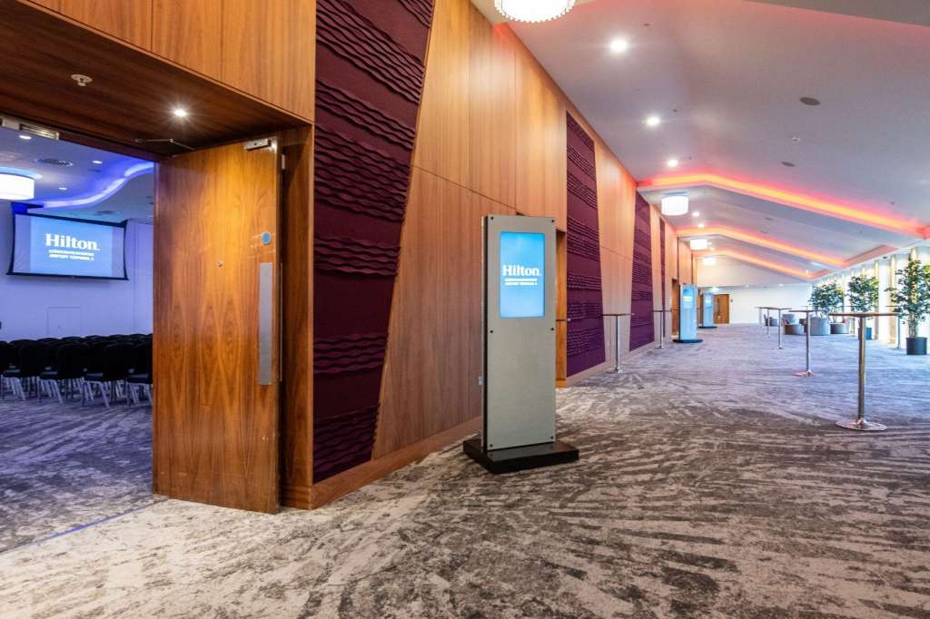 Modern ballroom corridor with wood paneling, ambient lighting, and branded wayfinding displays.