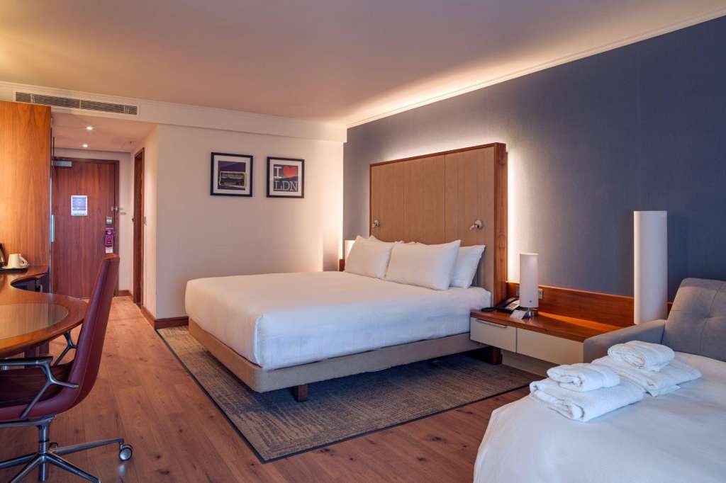 Hotel guest room with two beds, wooden furniture, desk area, and modern lighting.