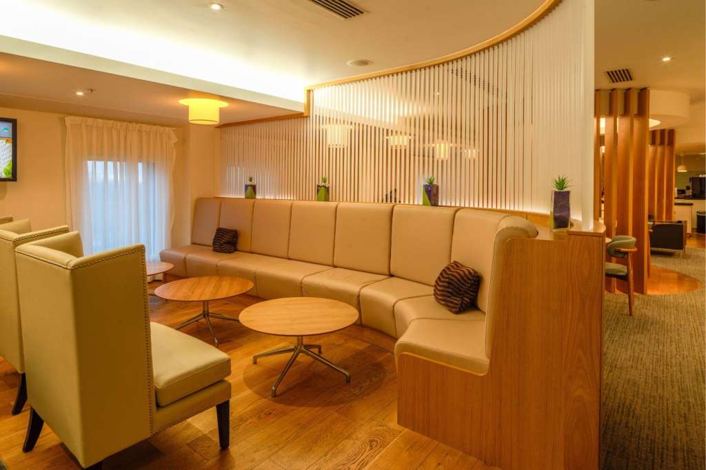 Modern lounge area with curved tan seating, round wooden tables, and vertical slat wall dividers.