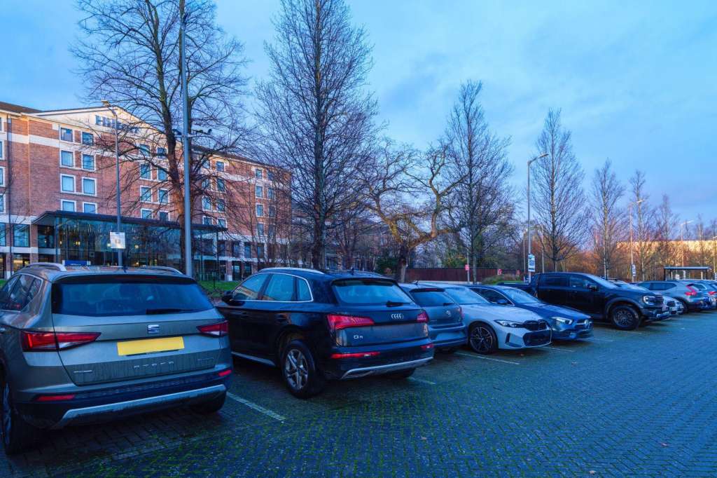 Exterior parking lot with parked cars, bare trees, and brick building in background.