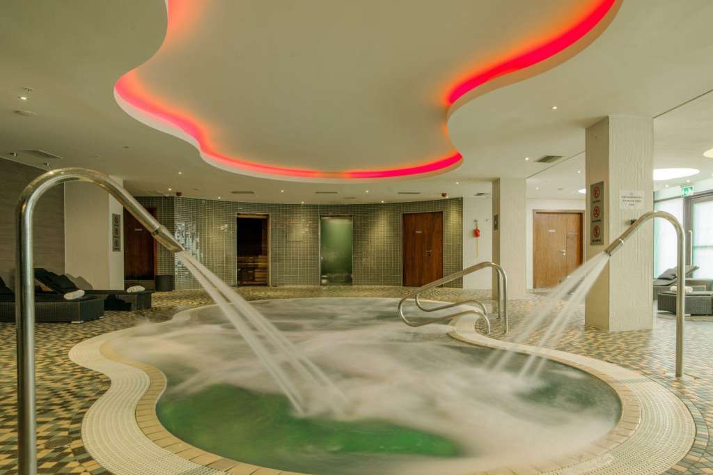 Indoor spa area with hot tubs, neon red ceiling lighting, tiled walls, and metal handrails.