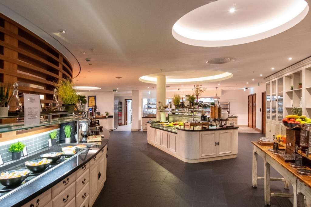 Modern catering kitchen with multiple prep stations, light wood cabinetry, and oval skylights overhead.