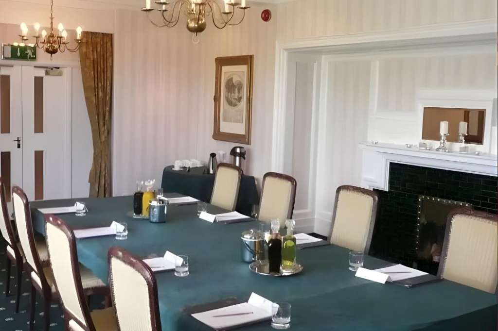 Meeting room with rectangular table dressed in teal cloth, place settings, brass chandeliers, and fireplace.