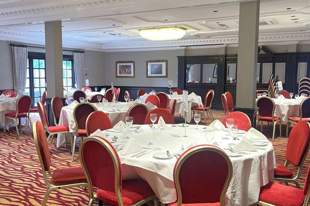 Ballroom set with round tables, white linens, red chairs, and place settings for formal dining.