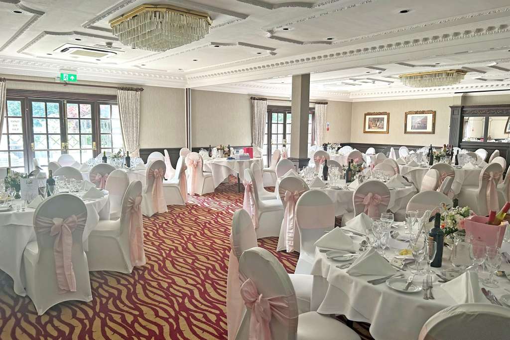Ballroom set up for a formal dinner with round tables, white chair covers, pink sashes, and crystal glassware.