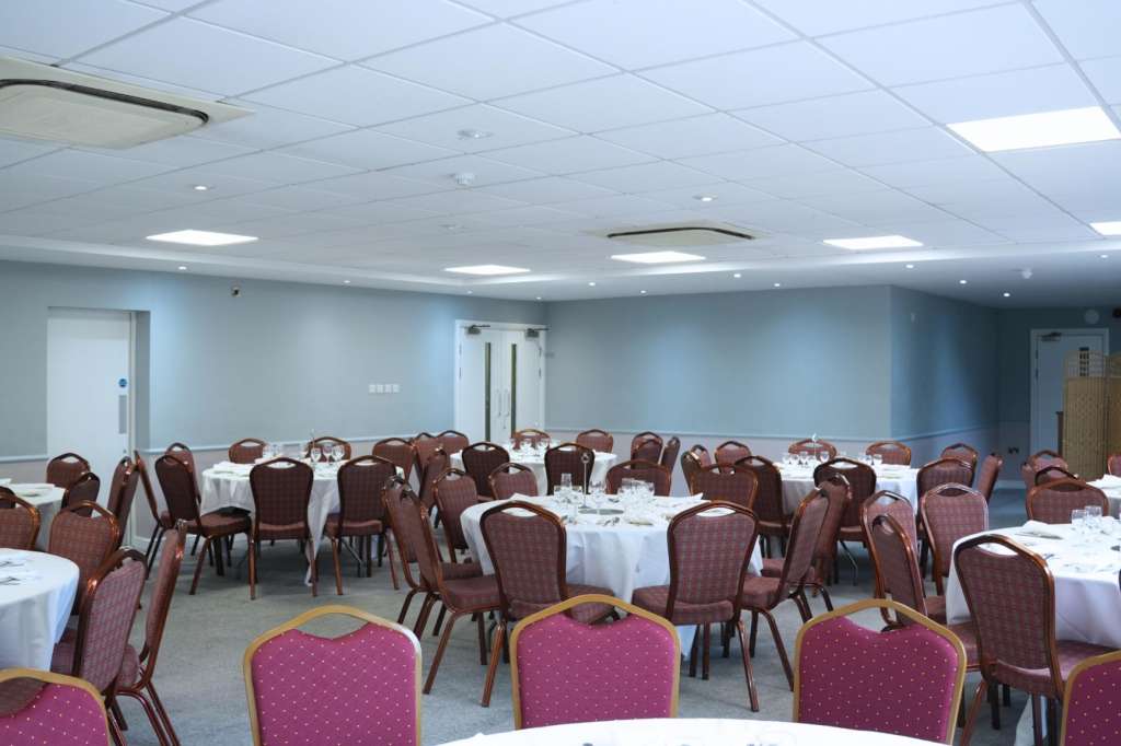 Banquet room with round tables dressed in white linens, burgundy upholstered chairs, and place settings.
