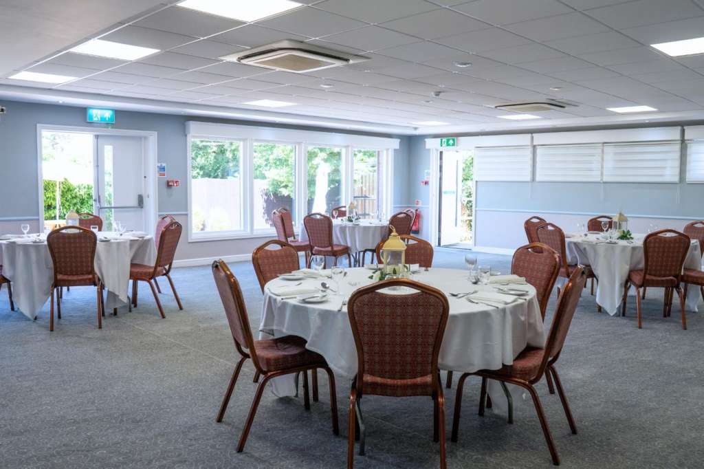 Banquet room with round tables dressed in white linens, burgundy chairs, and place settings arranged for a formal meal.