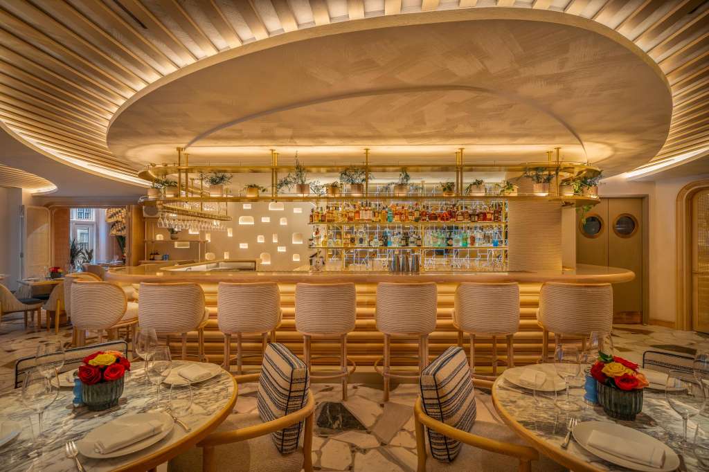 Bar and dining area with round tables, upholstered chairs, and illuminated ceiling feature with decorative greenery.
