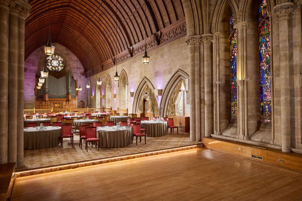Grand hall with vaulted ceiling, stained glass windows, organ, and round tables set for dining.