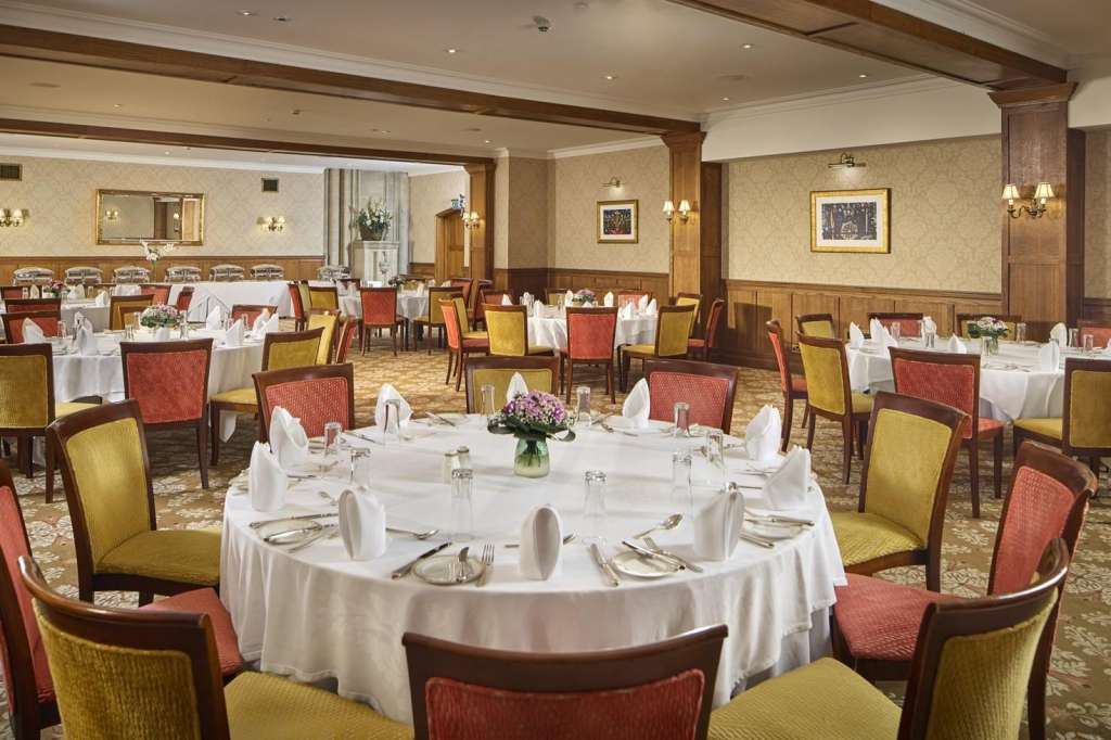 Ballroom set up for seated dining with round tables, white linens, and red and gold upholstered chairs.