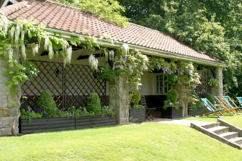 Summer House exterior with wisteria-draped pergola, manicured lawn, potted plants, and deck chairs.