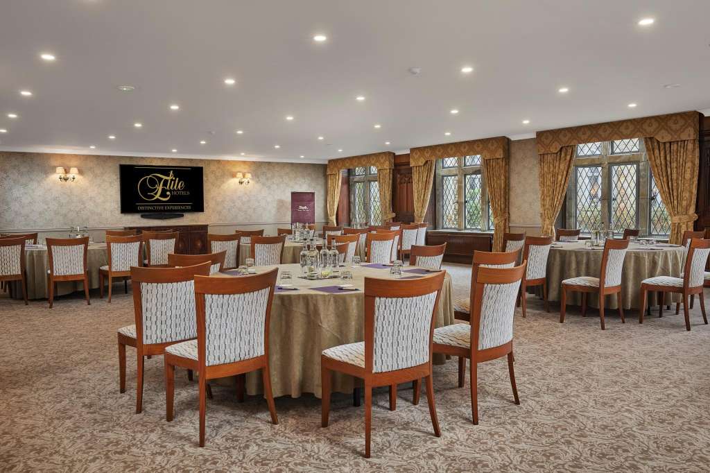 Elegant dining room with round tables, wooden chairs, gold tablecloths, and latticed windows with gold curtains.