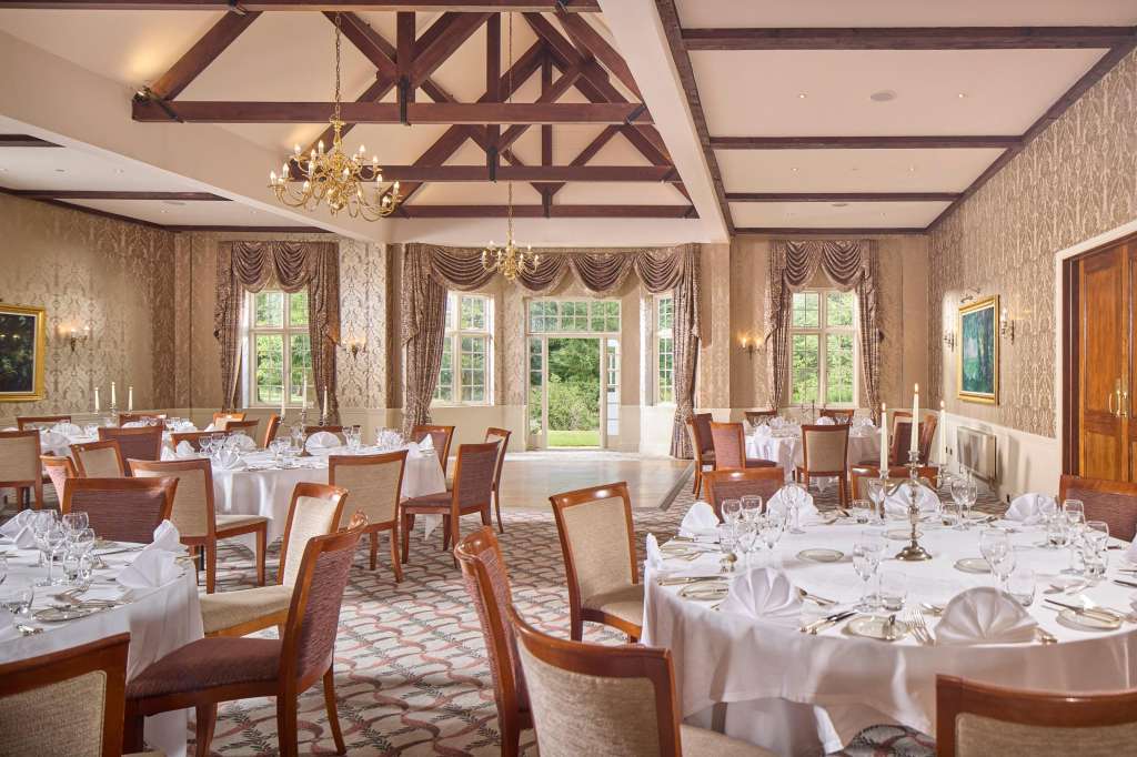 Elegant ballroom set for formal dinner with round tables, white linens, wooden chairs, and crystal chandeliers.