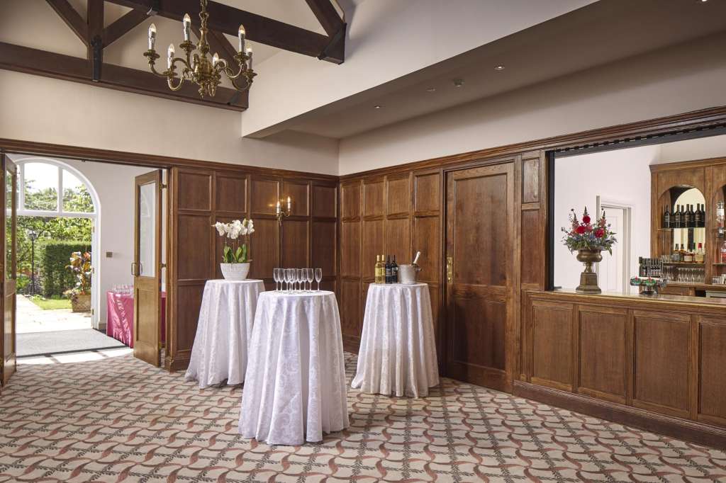 Elegant reception room with high ceilings, wood paneling, three cocktail tables with white linens, and a bar area.