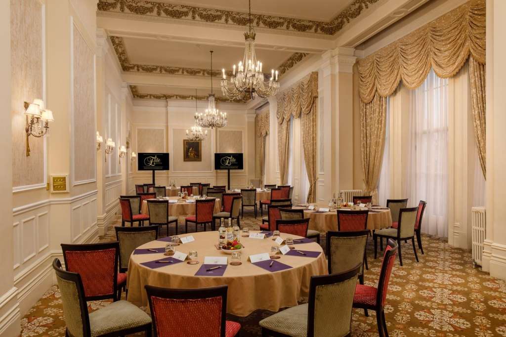 Elegant dining room with round tables set with gold linens, purple napkins, crystal chandeliers, and ornate gold drapes.