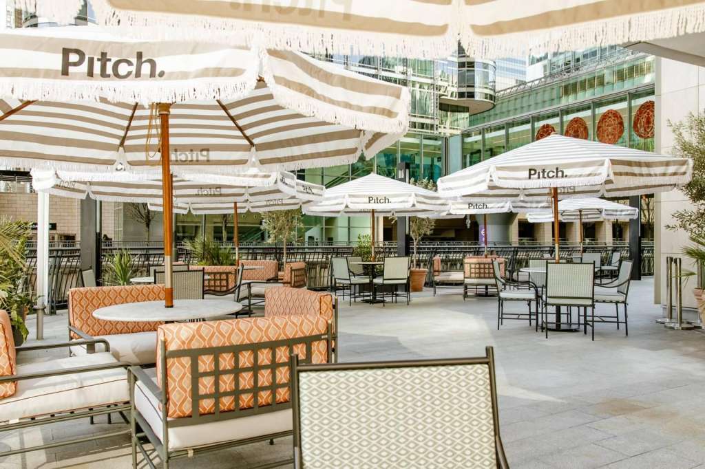 Outdoor rooftop terrace with striped umbrellas, lounge seating, and modern architectural backdrop.