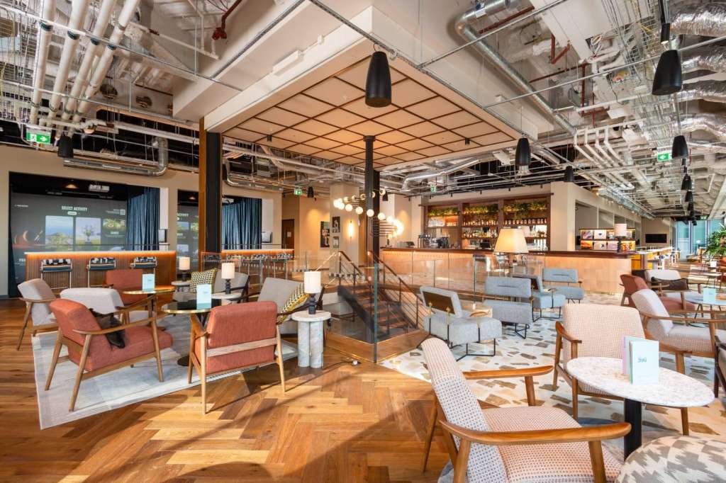 Modern lounge space with mid-century furniture, bar counter, geometric ceiling panels, and warm ambient lighting.