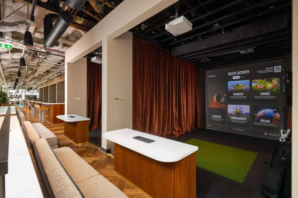 Modern event space with tiered seating, wooden desks, red curtains, and large interactive display screen showing activity options.