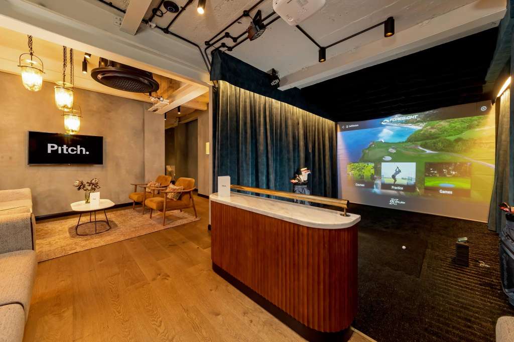 Modern meeting space with presentation screen, curved reception desk, lounge seating, and pendant lighting.