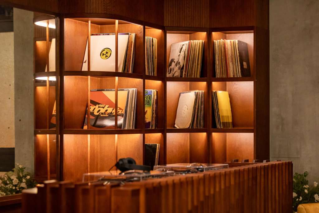 Illuminated wooden shelving display with vinyl records and artwork, modern interior styling.