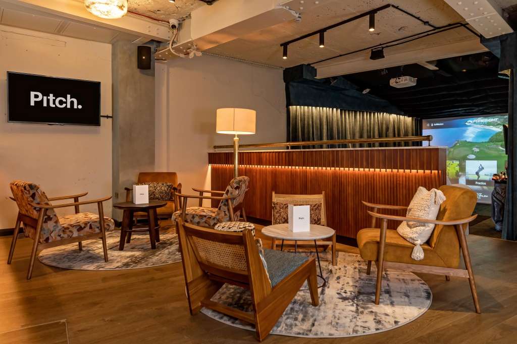 Modern lounge space with mid-century furniture, wooden accent wall, ambient lighting, and presentation screen.