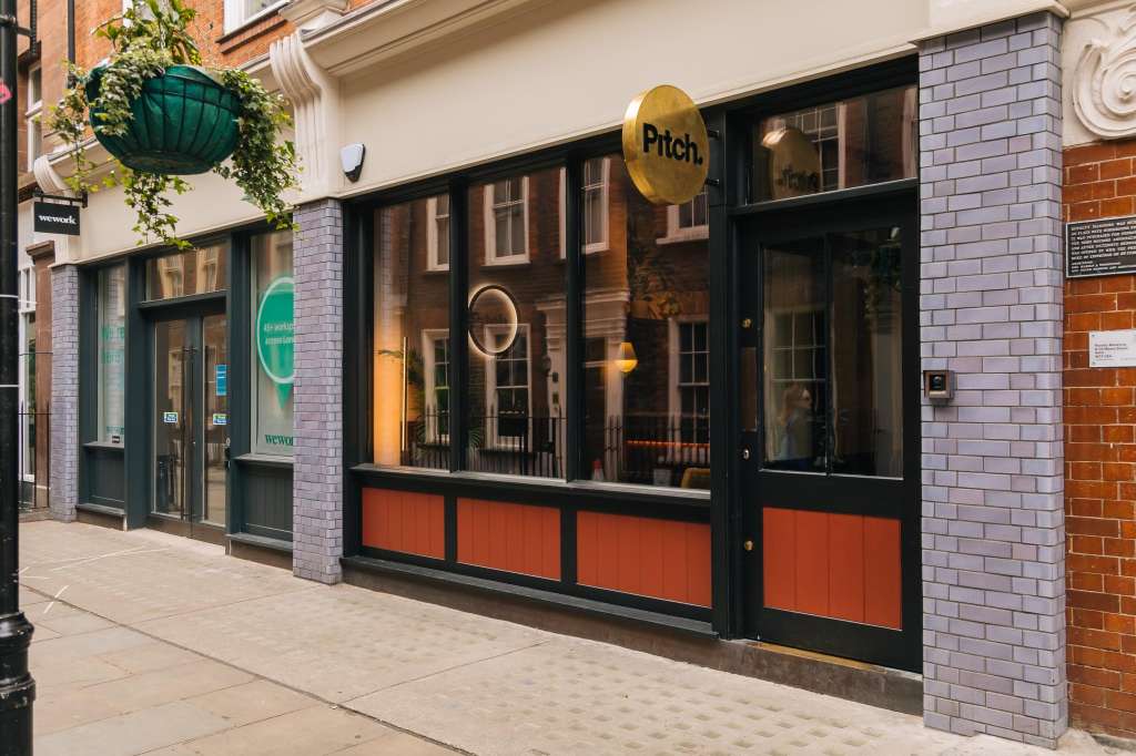 Exterior storefront of Pitch venue with black-framed windows, red panels, and hanging planters on brick facade.