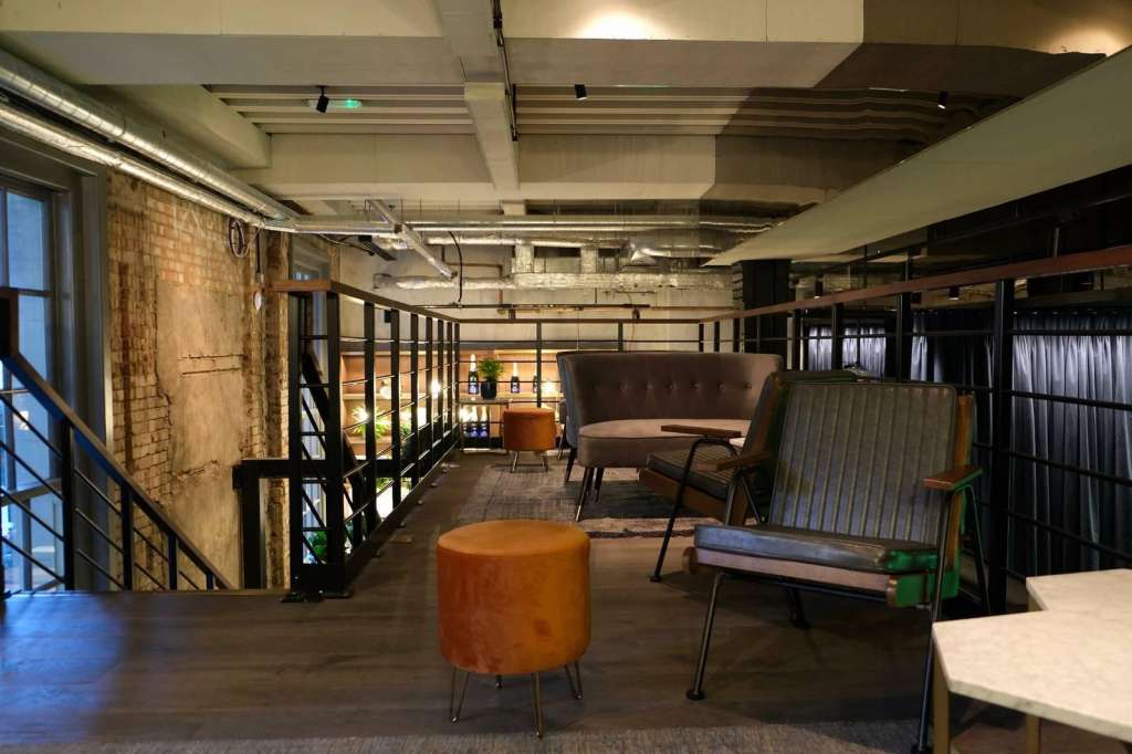 Industrial loft space with exposed brick, metal railings, modern seating, and polished concrete floors.