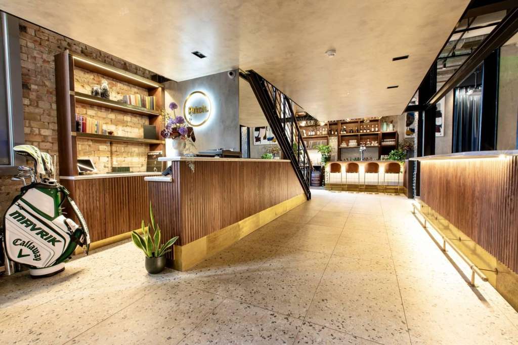 Modern corridor with wooden paneling, shelving, reception desk, and staircase. Polished concrete flooring and warm lighting throughout.