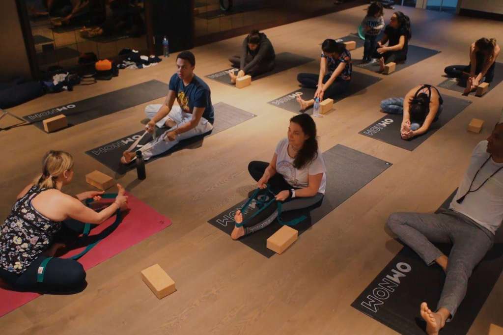 Group fitness or yoga class with participants on mats in a studio space with wooden flooring.